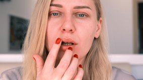 Portrait of a young girl applying a moisturizing balm to her lips. Beautiful blue-eyed blonde cares for her face, looking into the camera, slow motion, 4k - Powered by Shutterstock - Get 15% off with code: PIKWIZARD15