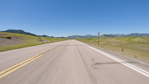 POV Driving a car on straight asphalt road in Montana. Sunny day with clear blue sky. Mountains in the background