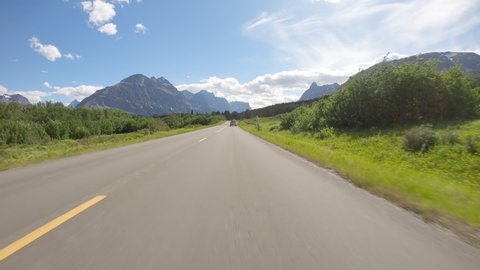 Riding a car on asphalt mountain road in Glacier National Park, Montana. Sunny day with blue sky and white clouds