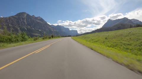 Driving a car on asphalt mountain road in Glacier National Park, Montana. Sunny day with blue sky and white clouds