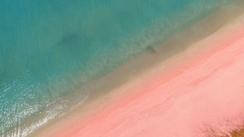 Amazing sea Aerial top view ocean blue waves break on pink sand beach waves crashing against an empty beach.Sea waves and beautiful pastel color romantic sand beach High quality video Bird's eye view