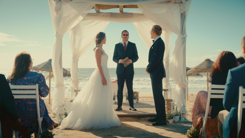 Beautiful Bride and Groom During an Outdoors Wedding Ceremony on a Beach Near the Ocean. Perfect Venue for Romantic Couple to Get Married, Kiss and for Friends with Multiethnic Cultures to Celebrate. Royalty-Free Stock Footage #1086693674