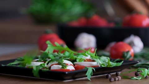 Delicious caprese salad with tomatoes, mozzarella, basil, cheese, pesto sauce, fresh arugula leaves. Pouring pesto sauce on Caprese lettuce slow motion. Healthy eating. Italian cuisine Vegetarian food