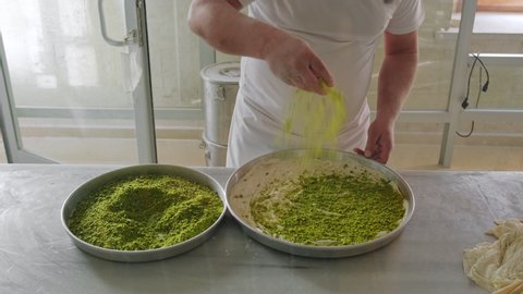 Chef covering freshly baked Turkish baklava with delicious ground pistachios, Gaziantep, Turkey. Cooking process close-up
