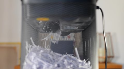 Sheets of A4 paper documents containing sensitive information are fed through a shredder machine