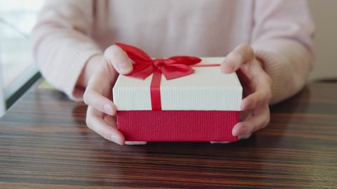 Presentation of a present for Valentine's Day, anniversary, birthday, Christmas. Close-up of a gift box in the hands of red and white with a ribbon. A romantic moment. High quality 4k footage.