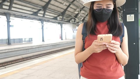 Woman passenger wearing face mask and using mobile phone at train station,Safety on public transport concept,New normal during covid-19 pandemic