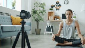 Young man is recording internet tutorial teaching yoga online using camera at home. Social media and creative young people concept.
