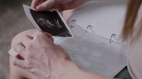 Close-up of a pregnant woman inserting an ultrasound scan of her baby into a photo album. Family values, a photo album with the first photo of the baby. 4k in slow motion