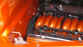 This panning video shows a close up view of a kustom orange hot rod's engine.