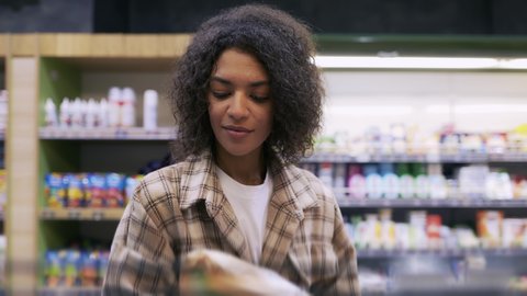 Curly woman taking corn flakes from the shelf, reads ingredients on packs