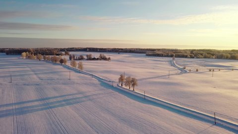 Iconic rural road under snow layer during golden sunset, aerial drone shot