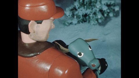 1950s: Marionette of a blue ox bows and pulls two sleds of sticks through snow covered woods. Slate. Man carries a blue calf and pets an ear. Hand pushes the puppet.