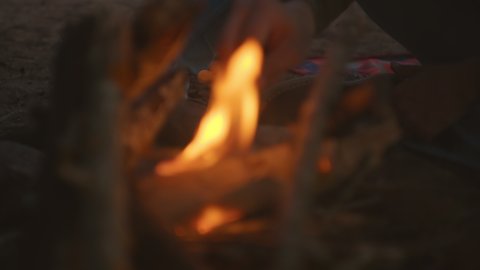 Close up on male hand poke inside camp fire with a stick. Camping outdoors on cold night. Warmth and cosy atmosphere from man made fire in forest. Enjoy outdoor lifestyle