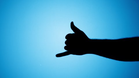 Shadow of Hawaiian shaka greeting gesture isolated on blue neon background. Showing hand gesturing with fingers close-up.