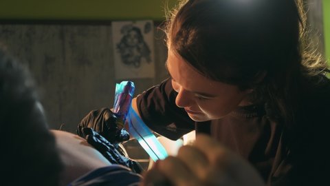 Female tattoo artist work with electric needle machine on customers shaved chest. Close-up of woman master tattooist in black gloves with polyethylene covered gun tattooing ink in bare clients body.