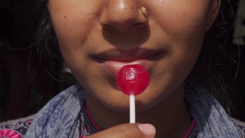 Beautiful young girl eating a red lollipop using his mouth on a dark background. Crop face close-up view.