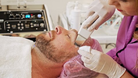  Cosmetologist making a mid age man a therapeutic procedure on a face  Man in a spa salon on cosmetic procedures for facial care.  Beautician using electrical impulses for facial procedures. 