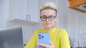 Networking online concept. Young woman with tom boy haircut using modern blue mobile phone and laptop for communication with clients. Freelancer person working at home during lockdown in 4k footage