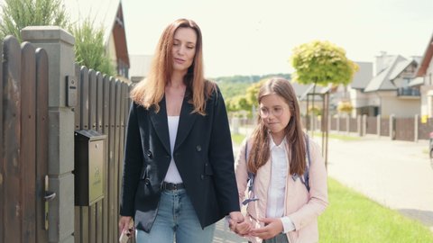 Portrait of beautiful mom in jacket and jeans holding her daughters hand and walking. Middle aged woman talking with her little child while going on way from school. Concept of family ralationship.