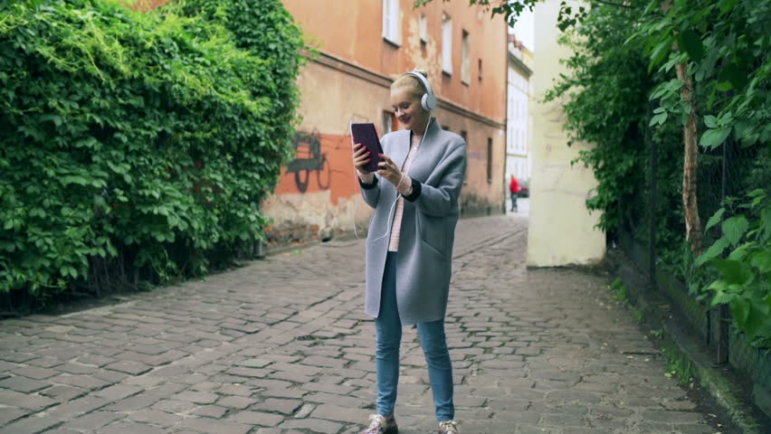 Happy girl listening music on tablet in the old street
