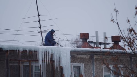 Nizhny Novgorod, January 27, 2022.  A man on the roof of an apartment building knocks down ice with a sledgehammer, knocking down icicles on the roof