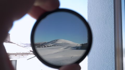 View of the snow-covered mountain peak through round tinted glass. The person holding camera 
ND filter and checking its opacity