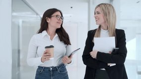 Video of two attractive young business women working with digital tablet while talking and walking in a modern startup.