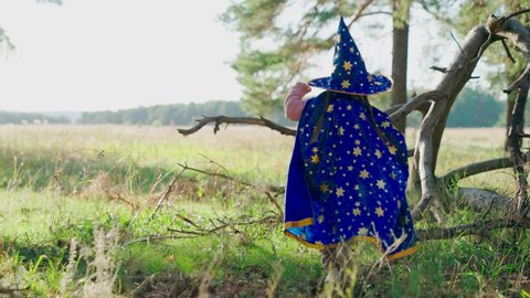 Fantasy child in wizards robe in forest. Kid play magician outdoors. Girl, kid, plays in wizard costume in spring in forest, studies dry tree. Halloween. Happy childhood, family. Child playing in park