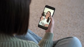 Young woman talking female doctor on smartphone by video calling at home. Psychotherapist waves hand beginning online consultation with client at videochat. People and psychology concept. 4k footage