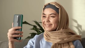 Dreamful young caucasian muslim woman in hijab hold use mobile cell phone , waving hand, video chatting with friend, doctor, family by smartphone. Islam religious concept. close up. 4k footage