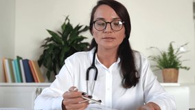 Female general practitioner give medical support to patient distantly use video call app, look at computer screen wear glasses, stethoscope and talk to client. Remote medicine consultation concept. 4k