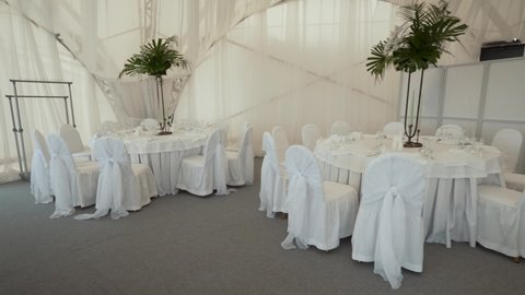 A large banquet hall on the ocean with large empty tables covered with white tablecloths