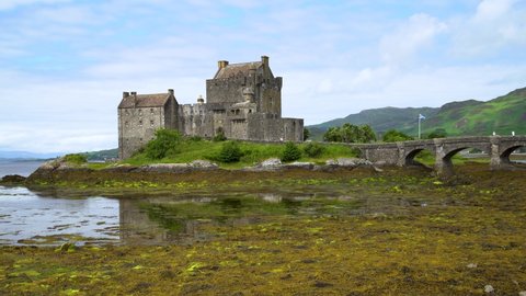 Very low tide at the beautiful Eilean Donan Castle as people walk over the historic bridge towards the fortress on a sunny summer day in Scotland. Low angle shot.