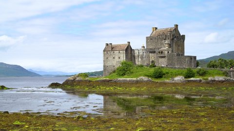 Several tourists pass in front of Eilean Donan Castle on a quiet summer day with the high hills of Scotland in the background. Low angle shot.