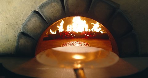 POV bakery worker taking hot cheesy pizza out of stone oven with peel. Point of view of cooking pizza with traditional recipe - food and drink close up 4k footage