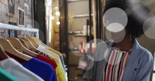 Animation of light spots over african american woman in clothes shop. global networks, business and connections concept digitally generated video.