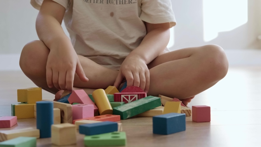 Angry boy destroys what he built from colorful figurines standing on the floor in the playroom. Child development.