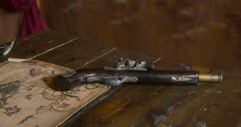 Pirate takes loaded revolver lying on wooden table near old sea yellowed treasure map IN cabin of pirate ship at voyage close view