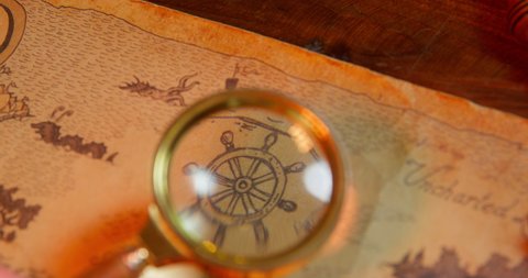 Pirate looks through big loupe at objects on sea treasure map lying on wooden table IN cabin OF pirates ship close view