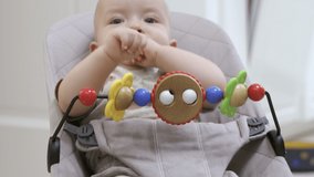 Toddler relaxing in a rocking chair with wooden toys on toy bar, cute baby boy using legs and arm muscles to spring up and down, child face close-up. High quality 4k footage