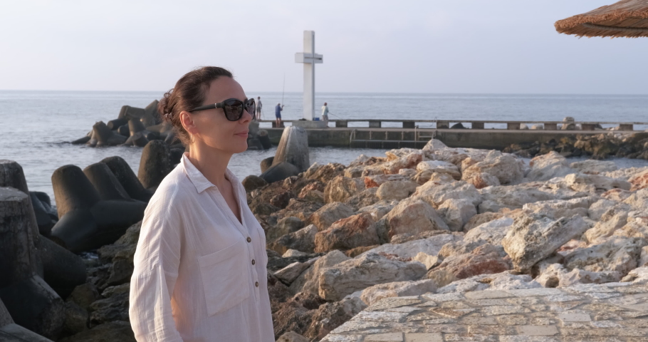 Woman look at sea rocks. A happy female enjoy the sea view on the beach with stones.