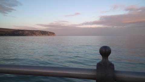 View out to sea from the end of a pier on Swanage beach in Dorset. Golden hour footage as sun is setting and seagulls float on the calm turquoise ocean.