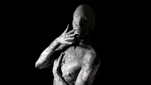 mysterious woman with blindfold and skin covered by clay is moving slowly in darkness