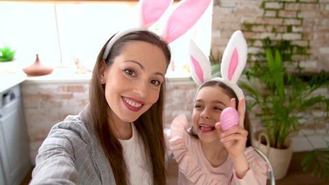 Mother and daughter doing selfie with Easter eggs, wearing bunny ears, have beauty and fun day together at home. Concept of childhood, happiness, family's weekend, friendship party. Domestic lifestyle