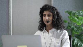 Close up smiling Indian young girl wearing headset with microphone, looking at web camera on laptop, studying online. Motivated Hindu tutor giving video call educational class.