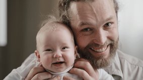Happy caucasian bearded dad and cute infant newborn girl kid daughter son talking to camera smiling talking laughting posingat home. Closeup father embracing little child video call looking at webcam