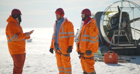 Coast guard team standing on frozen lake with hovercraft on background. Rescuers in safety uniform loading equipment in airboard preparing to patrol arctic area