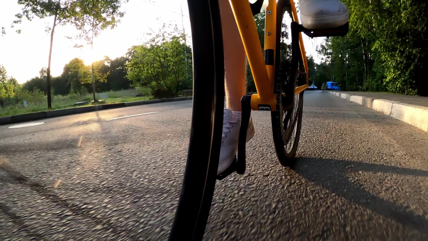 Legs of a cyclist quickly pedaling a bicycle that rides on the road in summer