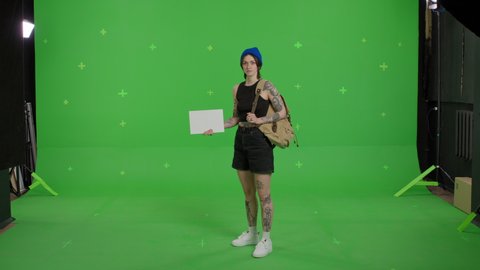 Young beautiful woman hitchhiking holding empty card . Young sexy girl looking for a ride to start a journey over green screen background. Summer time on Chroma Key. 4k uhd video footage